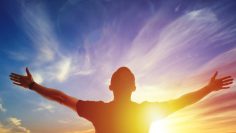 Young man standing outstretched at sunset. Bright solar glow and sky